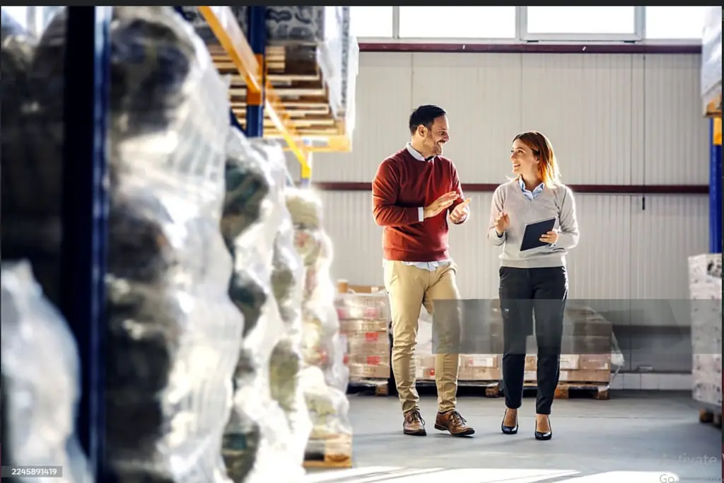 Two logistics team members reviewing inventory data on a tablet in a warehouse aisle