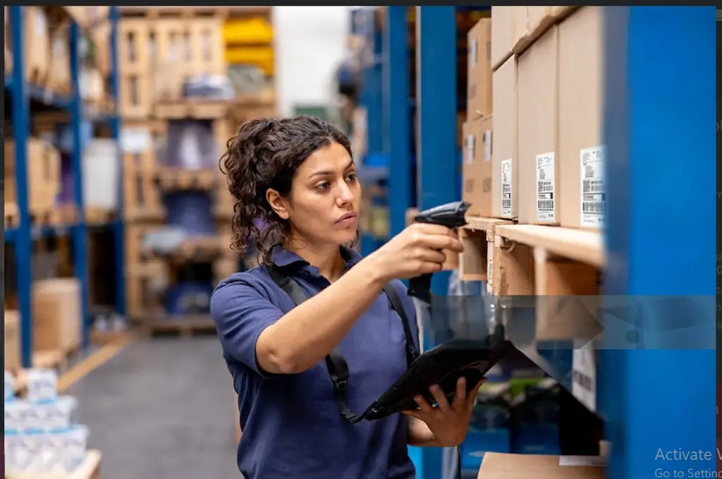 Warehouse operative scanning barcodes on stacked inventory with a handheld device